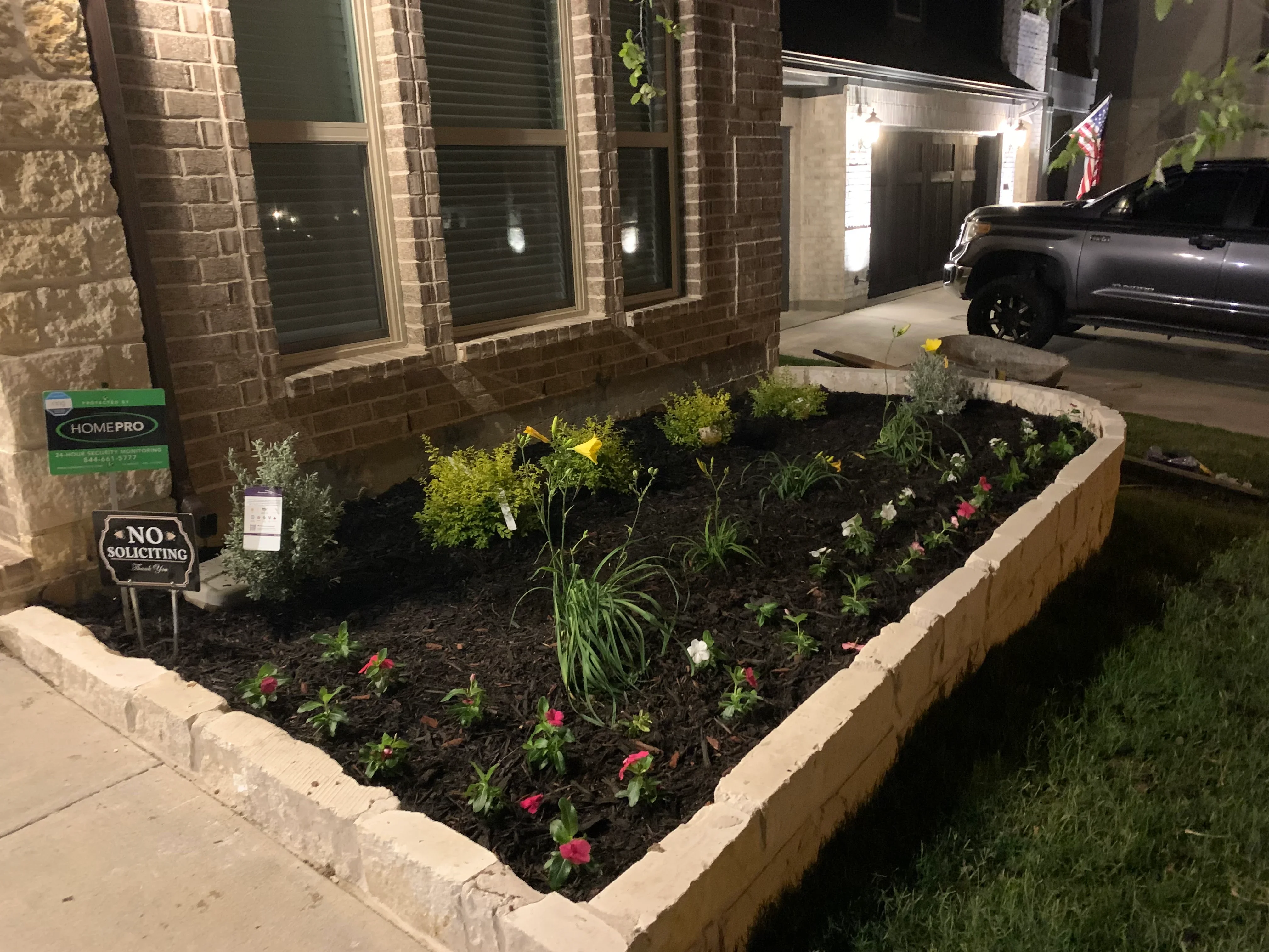 Concrete-edged planting bed with mixed perennials, ornamental grasses, and mulch along brick home foundation