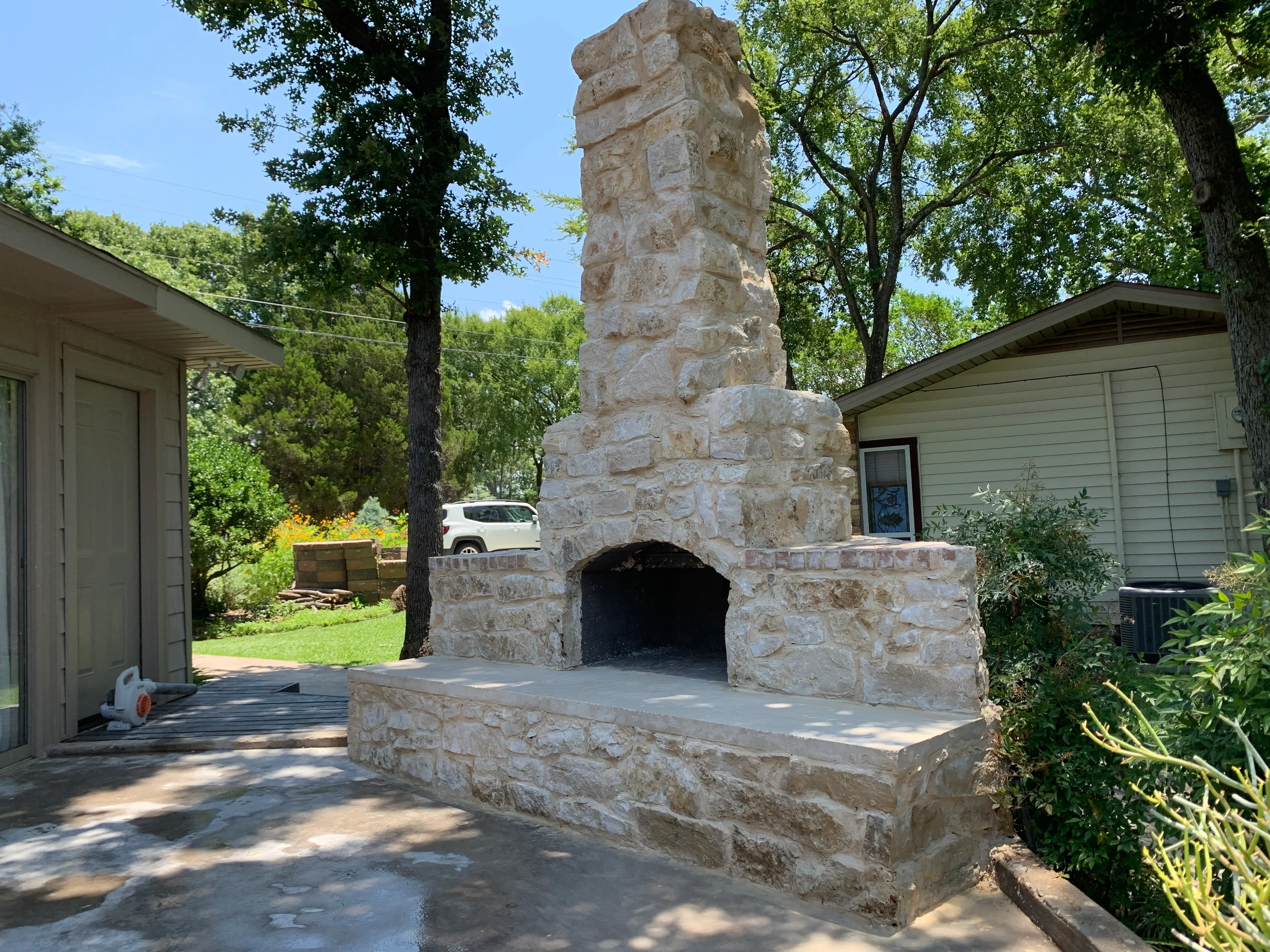 Stacked limestone fireplace with arched opening and concrete pad foundation in residential setting