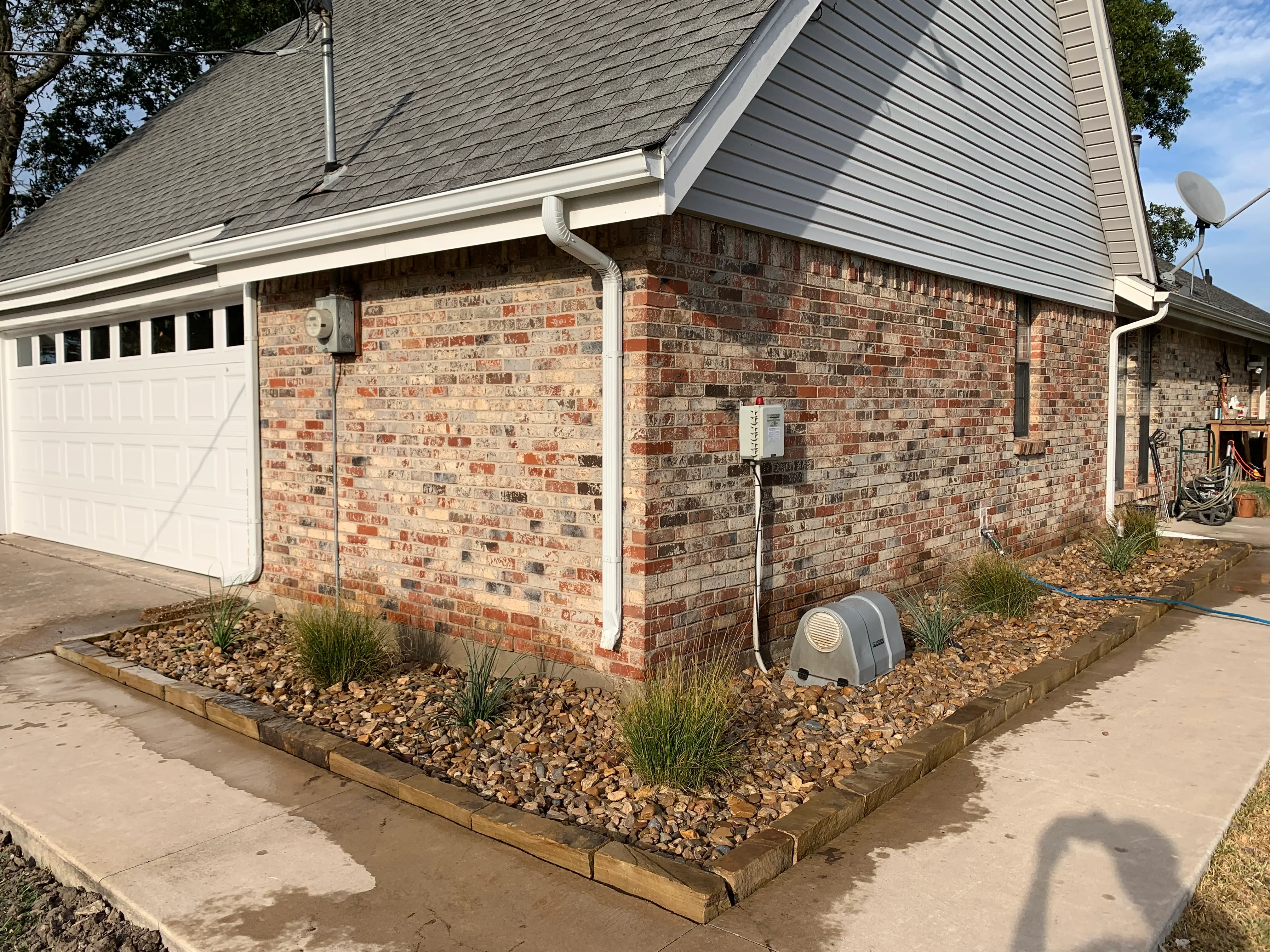 Brick foundation with river rock landscaping, ornamental grasses, and wood edging
