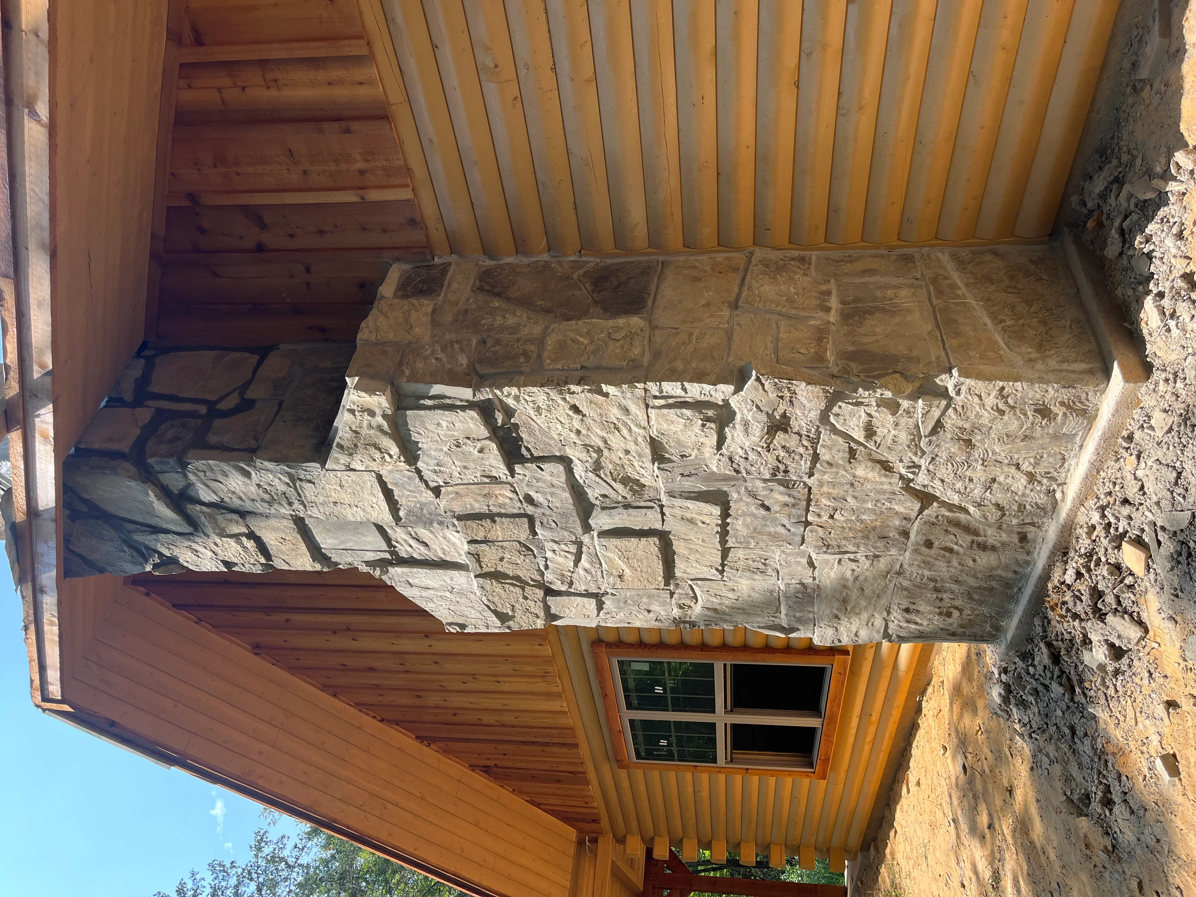 Stacked stone veneer wall with wood framing, soffit, and window opening
