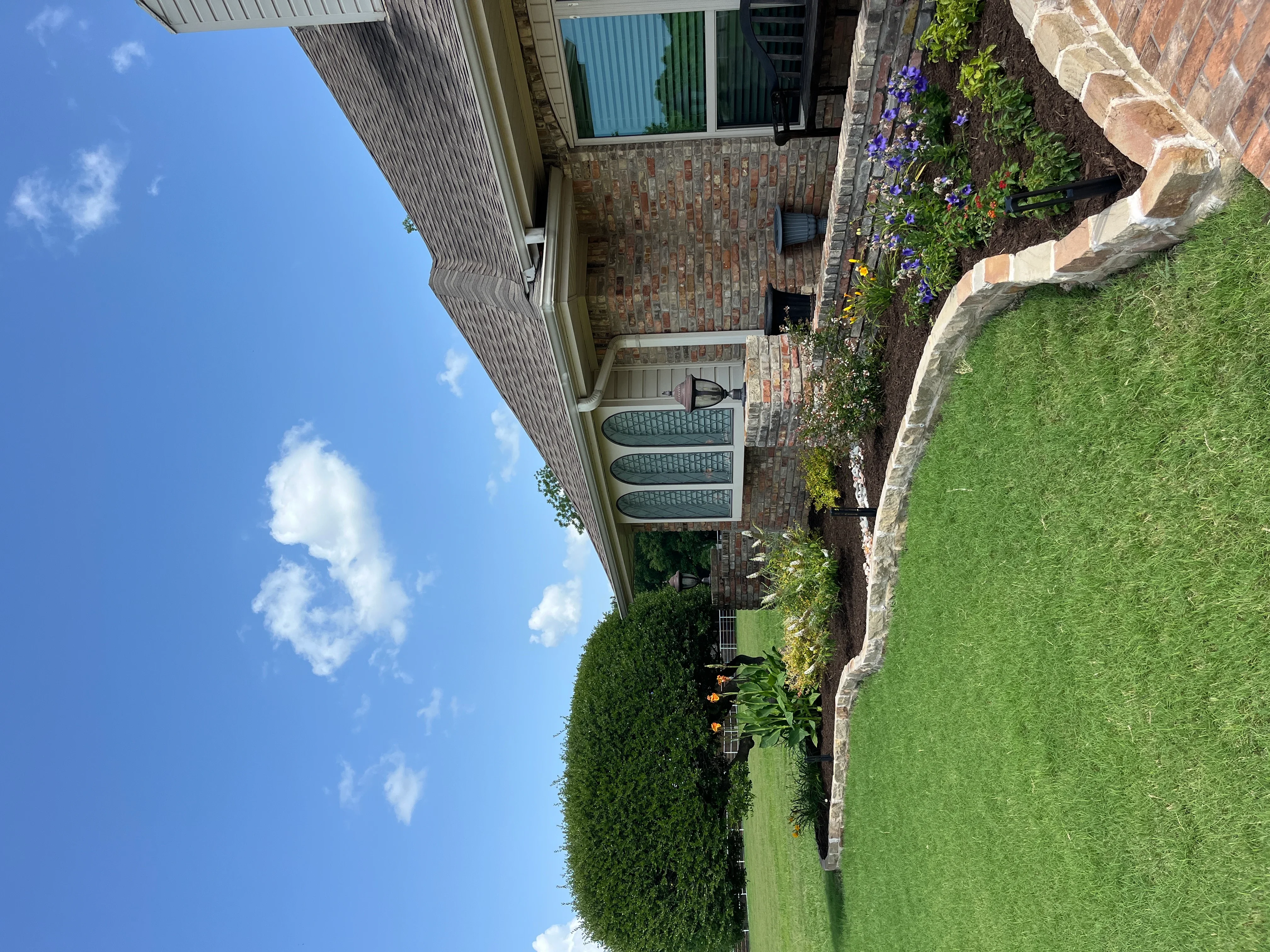 Brick paver patio with lawn, flowering plants, and hedges in residential backyard