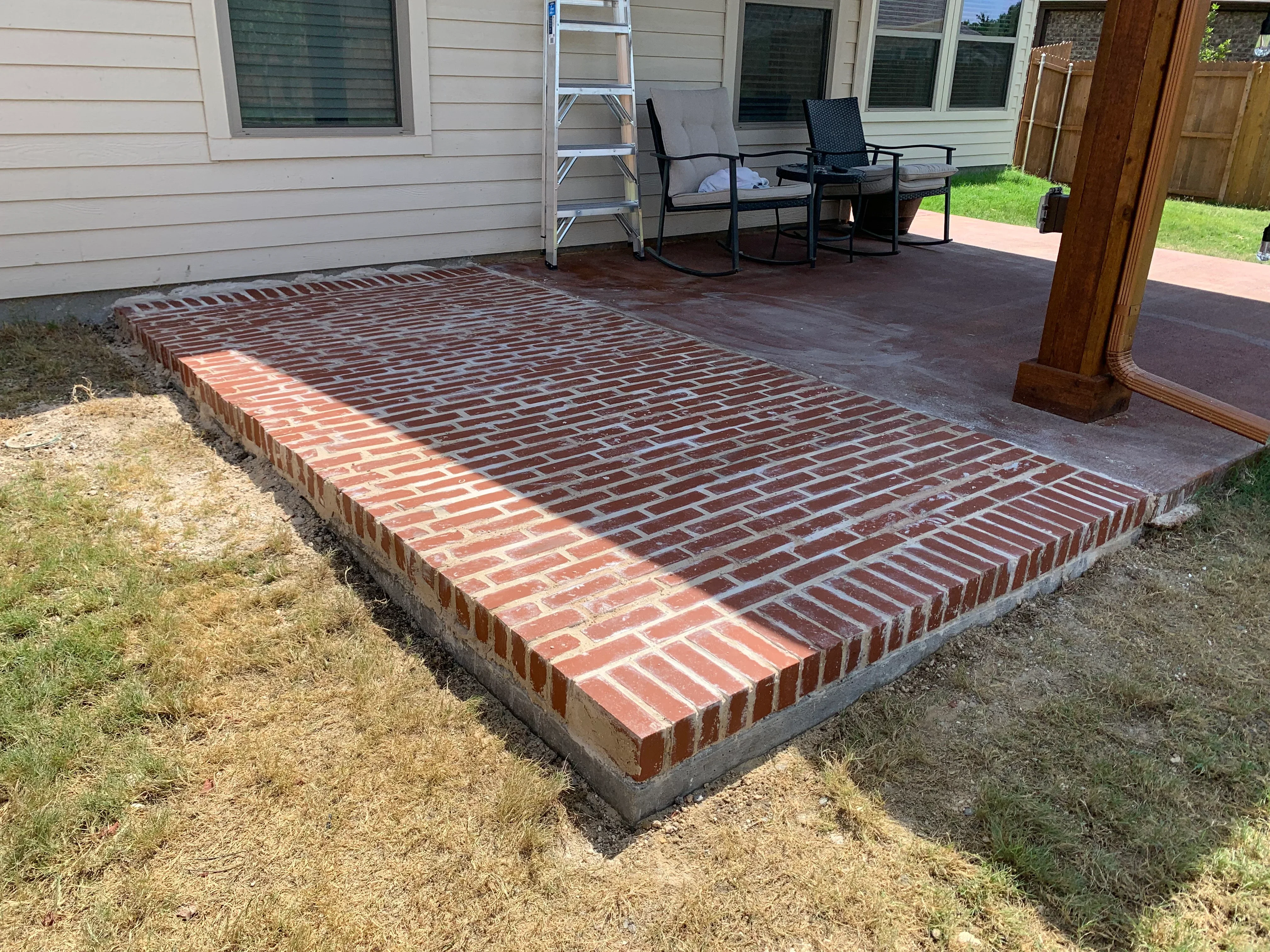 Red brick patio with running bond pattern and concrete foundation, adjacent to house and deck