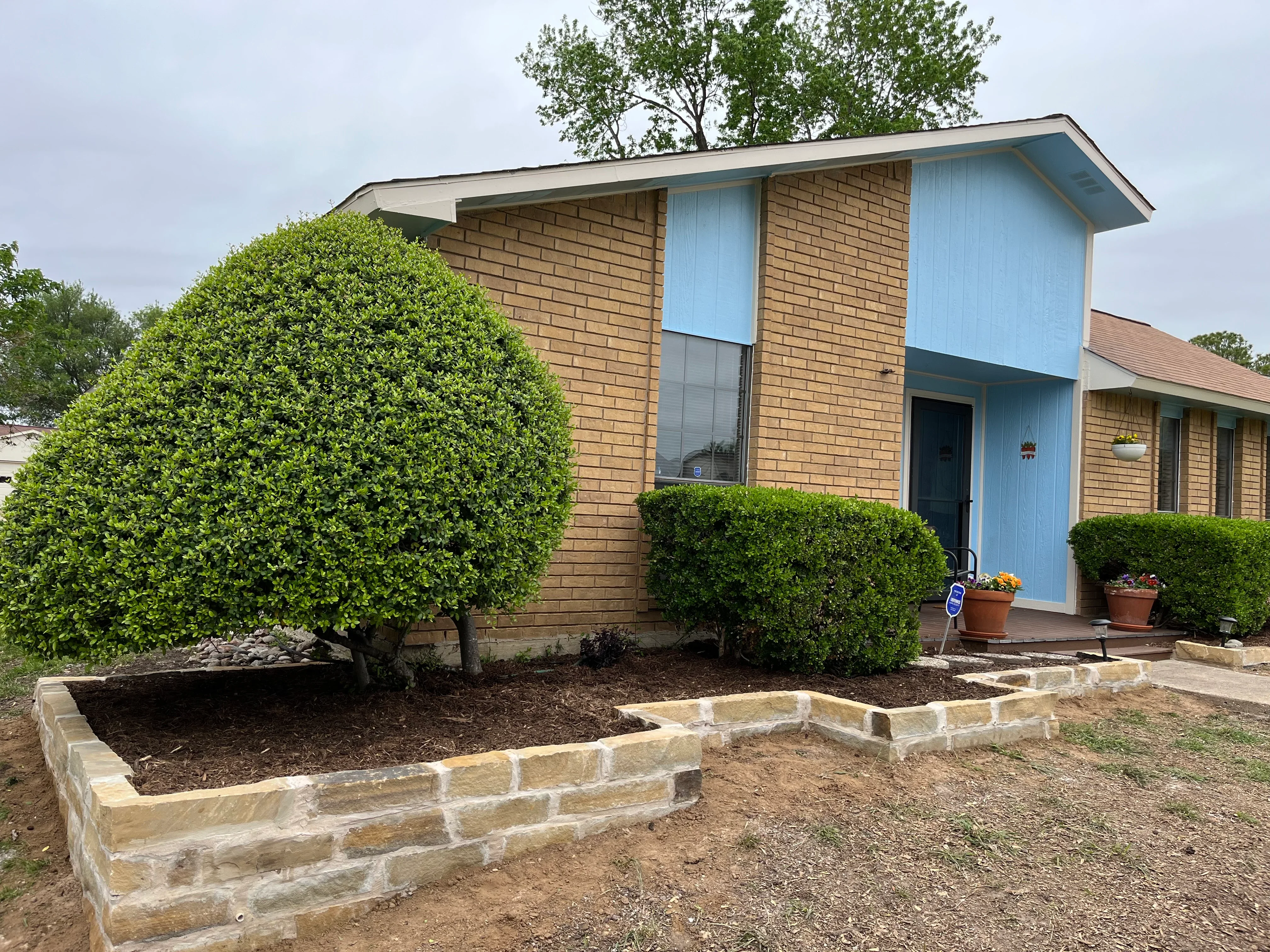 Stone-edged landscape beds with mulch and boxwood shrubs in front of brick home